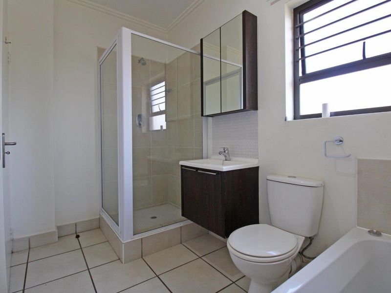 A clean, functional bathroom featuring a glass-enclosed shower, a separate bathtub, a wall-mounted vanity with a mirrored cabinet, and neutral floor tiling.