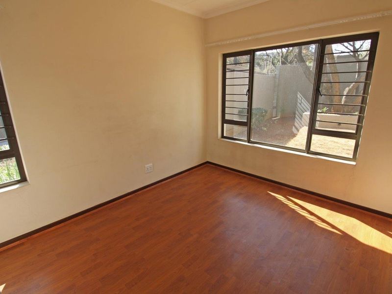 An empty bedroom featuring laminate flooring, large windows with security bars, and neutral wall finishes, offering a blank canvas for personalization.