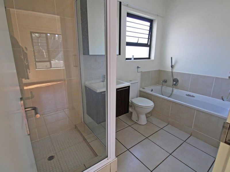 A functional bathroom featuring a separate shower enclosure, bathtub, toilet, and vanity basin with neutral tiled finishes.