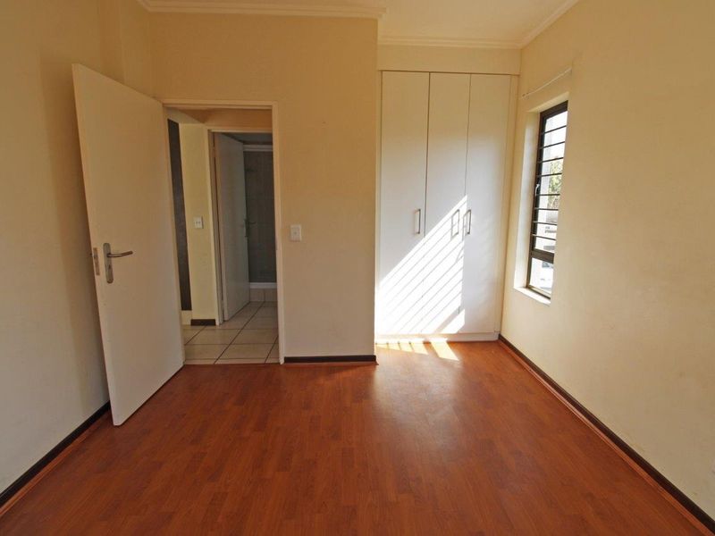 An empty bedroom featuring laminate flooring, a built-in wardrobe, and access to an adjoining bathroom.