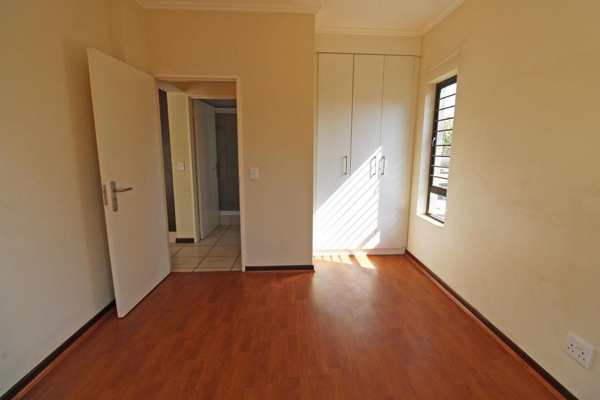 An empty bedroom featuring laminate flooring, a built-in wardrobe, and access to an adjoining bathroom.