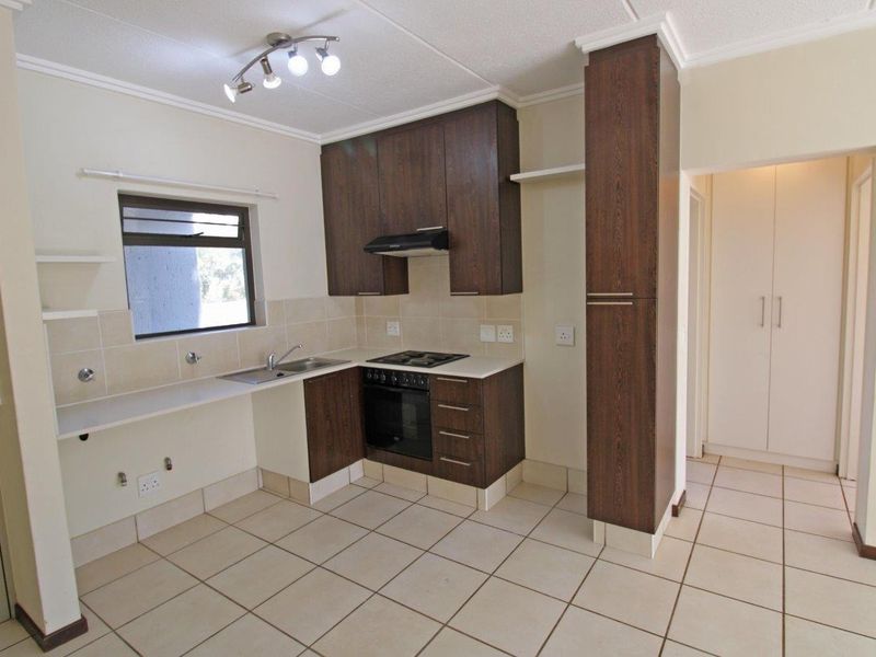 A clean, functional kitchen featuring dark wood cabinetry, built-in oven and hob, tiled flooring, and a neutral tiled backsplash.