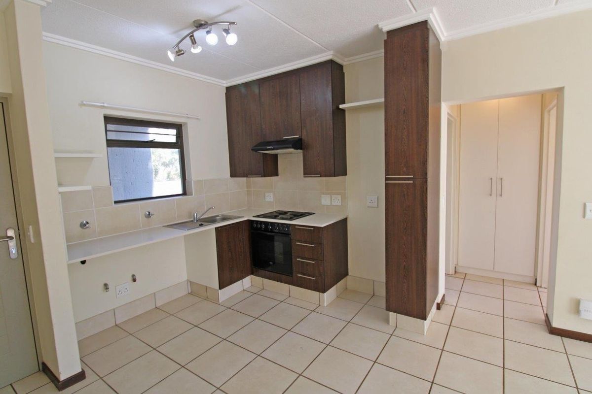 A clean, functional kitchen featuring dark wood cabinetry, built-in oven and hob, tiled flooring, and a neutral tiled backsplash.