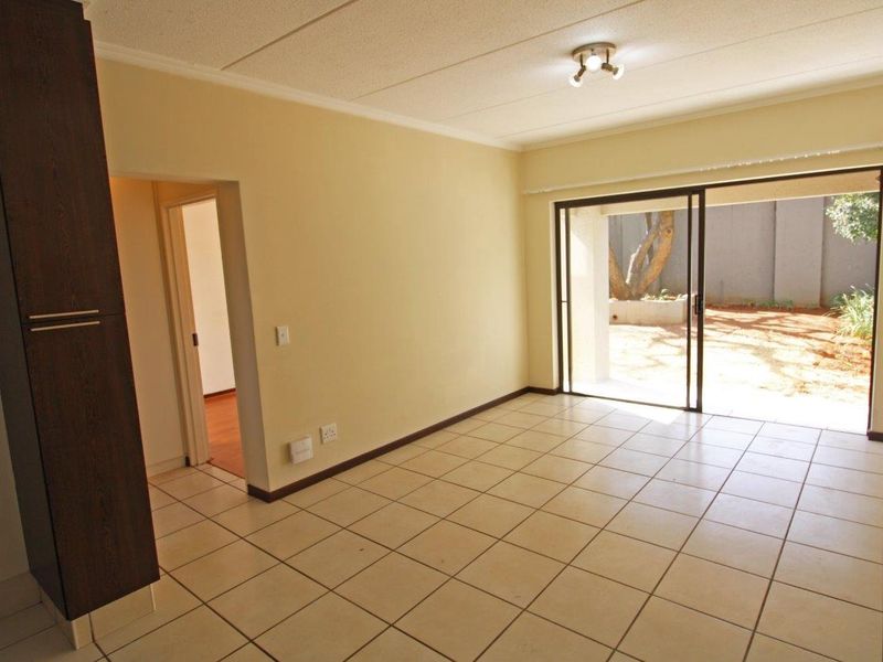An empty living room featuring tiled flooring, a built-in cupboard, and a sliding glass door providing access to an outdoor area.