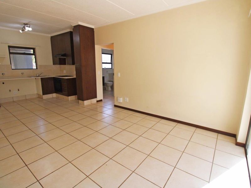 An open-plan living and kitchen area featuring tiled flooring, dark wood cabinetry, and integrated appliances, leading to an adjacent bathroom.