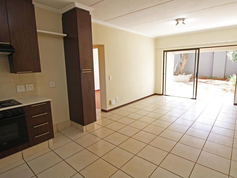 Open plan living area featuring tiled floors, a compact kitchen with built-in cabinetry and stove, and sliding doors leading to an outdoor space.
