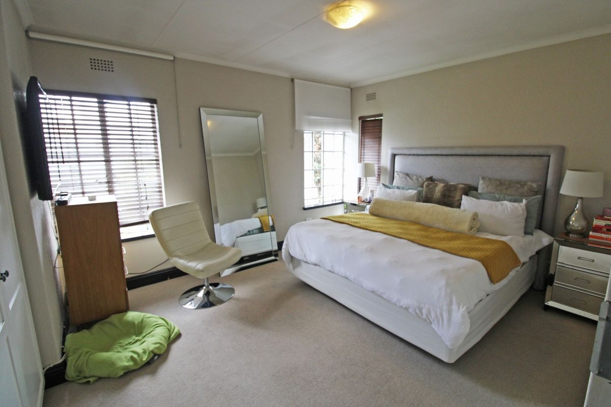A spacious bedroom featuring neutral carpeting, venetian blinds, and a wall-mounted television, offering a comfortable and functional living space.