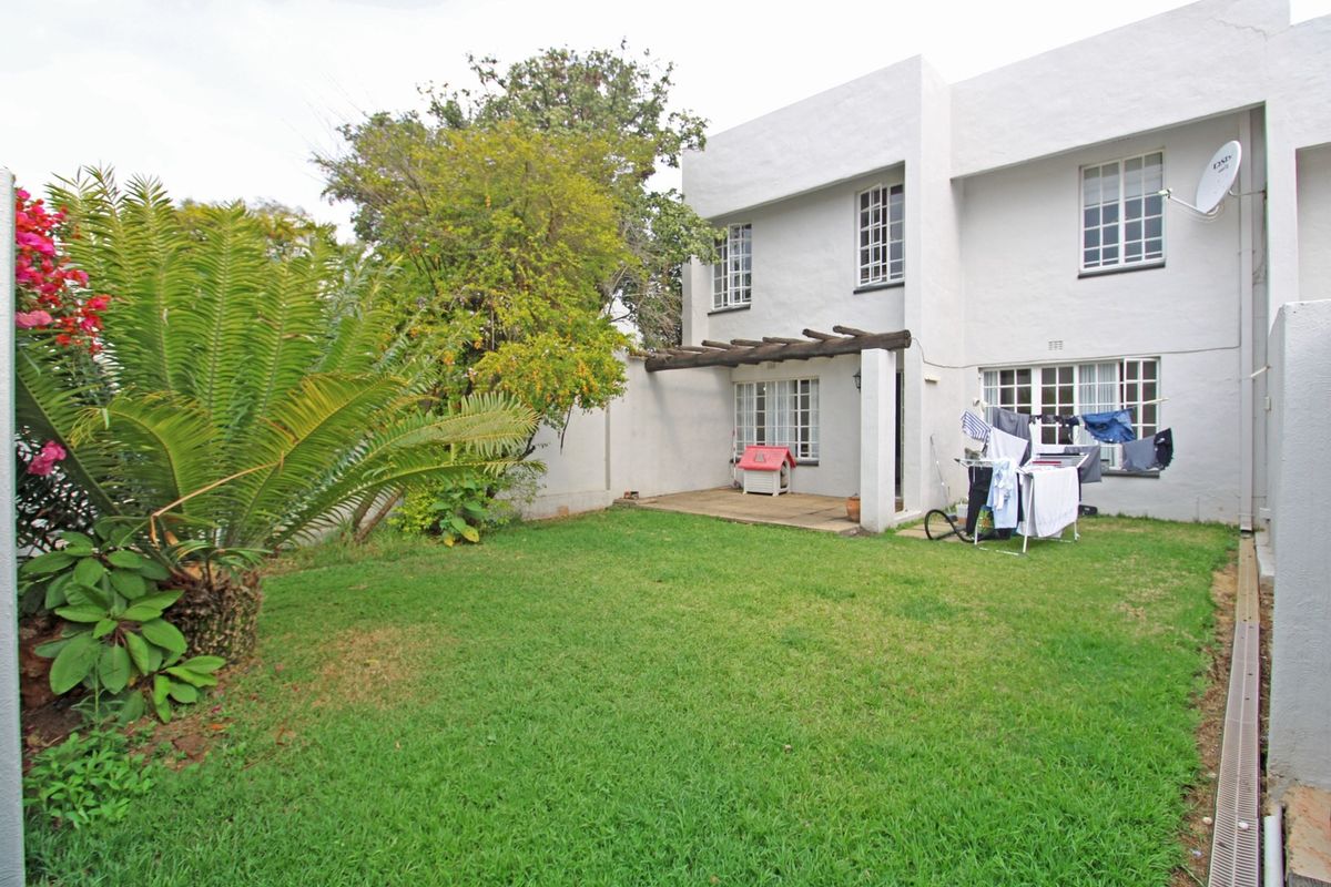 Rear view of the townhouse featuring a private garden, a paved patio area with a timber pergola, and established landscaping.