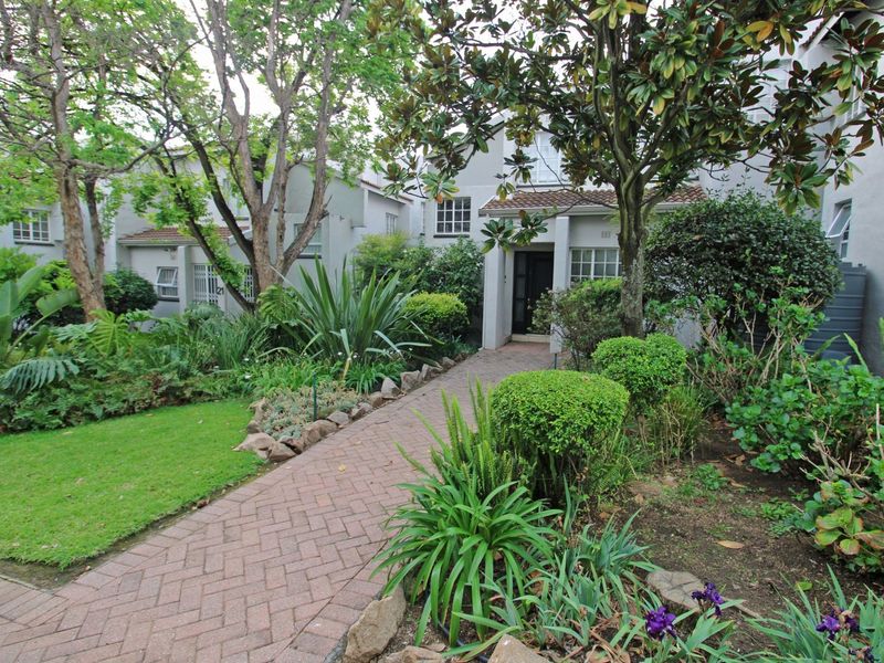 Front entrance of the townhouse featuring a brick paved walkway leading to the front door, surrounded by a well-established landscaped garden.