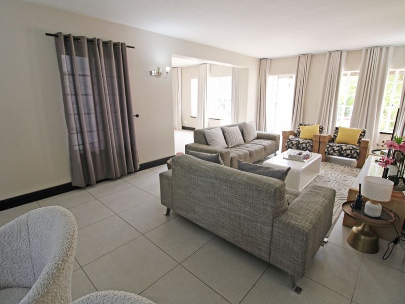 Spacious living room featuring neutral tiled flooring, wall-mounted lighting, and large windows with curtain tracks, offering a bright and open atmosphere.