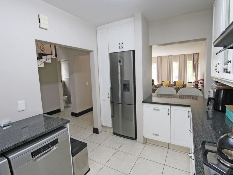 A functional kitchen featuring granite countertops, white cabinetry, and stainless steel appliances, with an open-plan layout connecting to the living area.