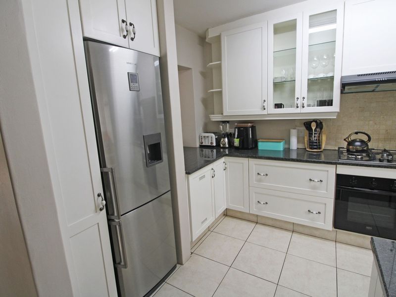 A well-maintained kitchen featuring white cabinetry, granite countertops, a gas hob, built-in oven, and tiled flooring.