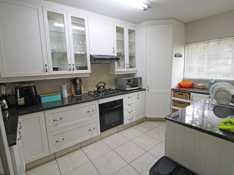 A well-maintained kitchen featuring white cabinetry, granite countertops, a gas hob, built-in oven, and tiled flooring with ample storage space.