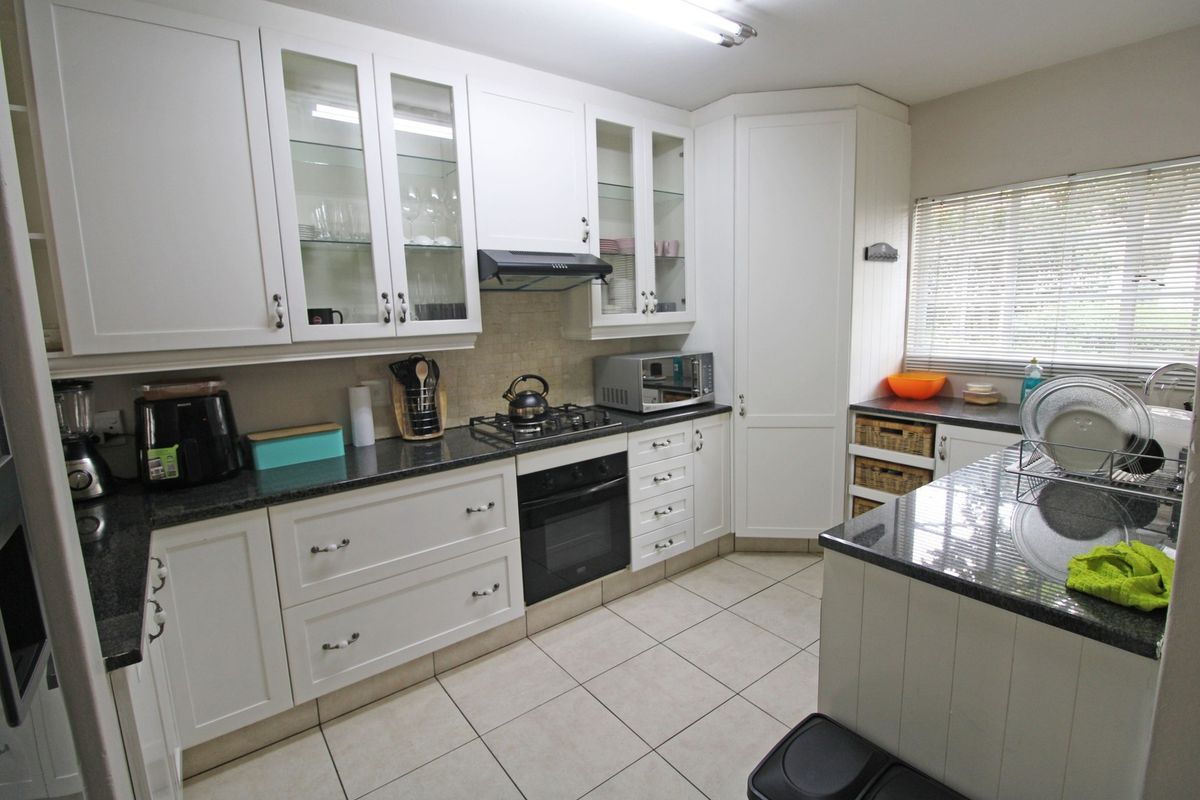 A well-maintained kitchen featuring white cabinetry, granite countertops, a gas hob, built-in oven, and tiled flooring with ample storage space.