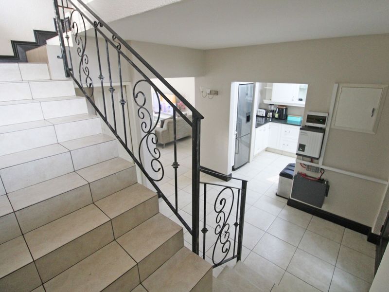 Open plan interior view featuring a tiled staircase with wrought iron railing, leading down to a kitchen area with built-in cabinetry and inverter system.