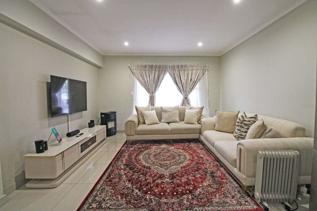 A well-maintained living room featuring neutral tiled flooring, recessed downlighting, and decorative coving, creating a bright and comfortable space.