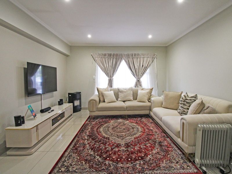 A well-maintained living room featuring neutral tiled flooring, recessed downlighting, and decorative coving, creating a bright and comfortable space.