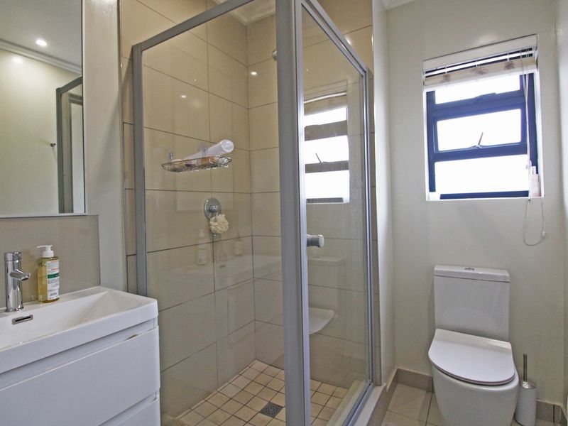 A clean and functional bathroom featuring a glass-enclosed shower, modern vanity basin, and toilet with neutral wall and floor tiling.