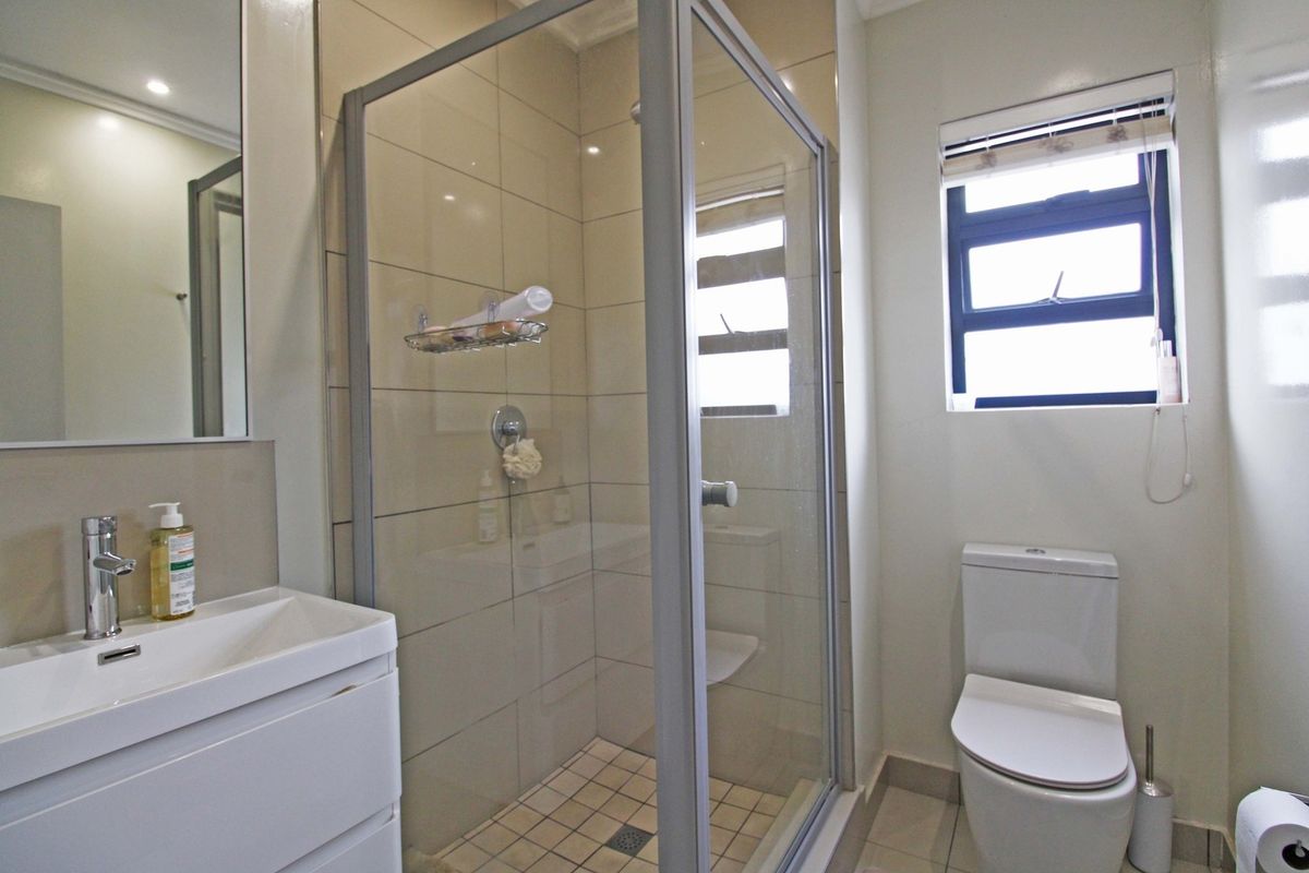 A clean and functional bathroom featuring a glass-enclosed shower, modern vanity basin, and toilet with neutral wall and floor tiling.