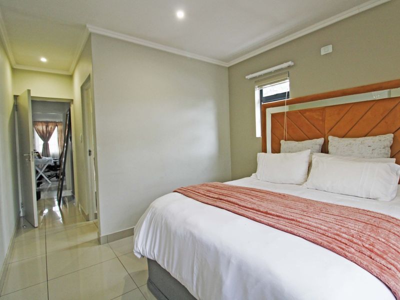 A well-maintained bedroom featuring neutral wall tones, tiled flooring, recessed downlighting, and a window fitted with a roller blind.