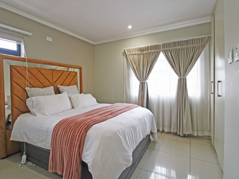 A well-maintained bedroom featuring neutral tiled flooring, built-in cupboards, and recessed ceiling lighting, offering a clean and functional living space.