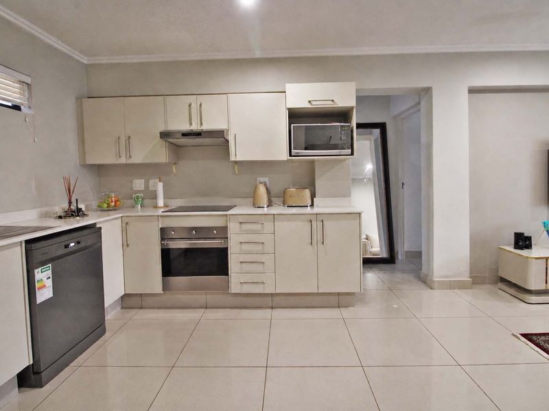 Modern open-plan kitchen featuring neutral cabinetry, built-in appliances, and sleek tiled flooring, seamlessly flowing into the adjacent living area.