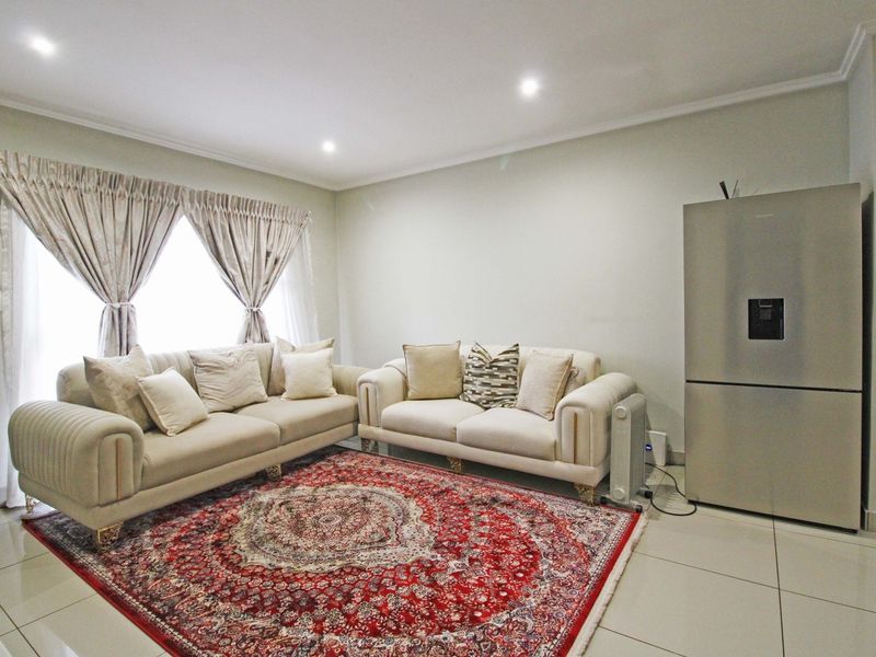A bright living room featuring neutral tiled flooring, recessed downlighting, and large windows with installed curtain tracks.