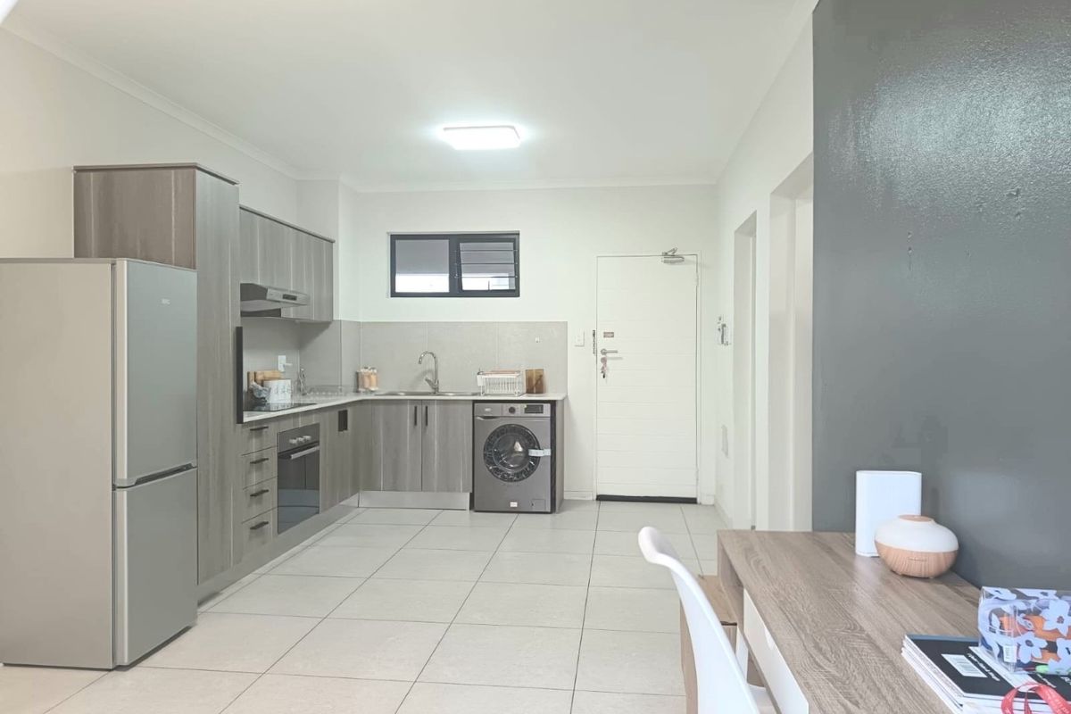 Modern open-plan kitchen featuring sleek grey cabinetry, built-in oven, extractor fan, and tiled flooring, seamlessly integrated with the living area.