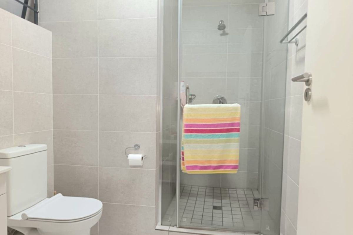 A modern bathroom featuring a glass-enclosed shower, neutral wall tiling, and a standard toilet suite.