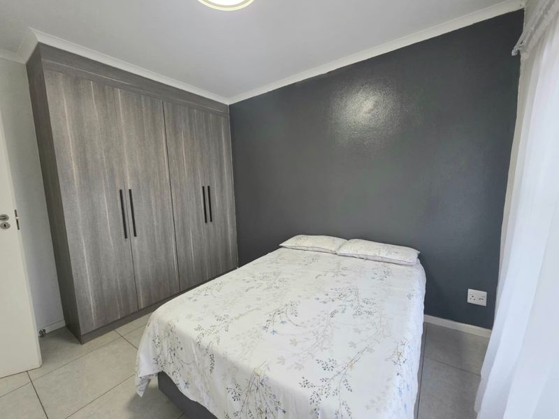 A well-maintained bedroom featuring modern grey built-in cupboards, neutral tiled flooring, and a dark accent wall.