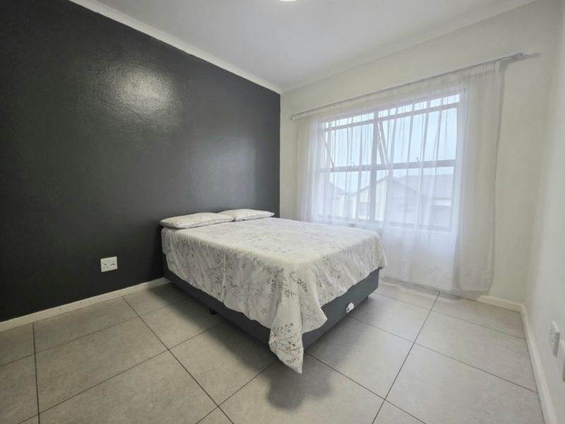 A bright bedroom featuring neutral tiled flooring, a dark accent wall, and a large window allowing for ample natural light.