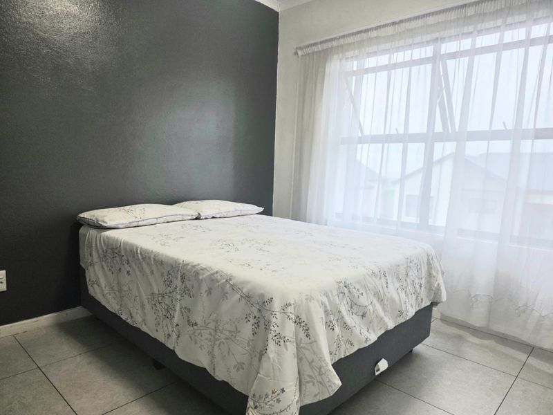 A bedroom featuring tiled flooring, a large window with sheer curtains, and a dark grey accent wall.