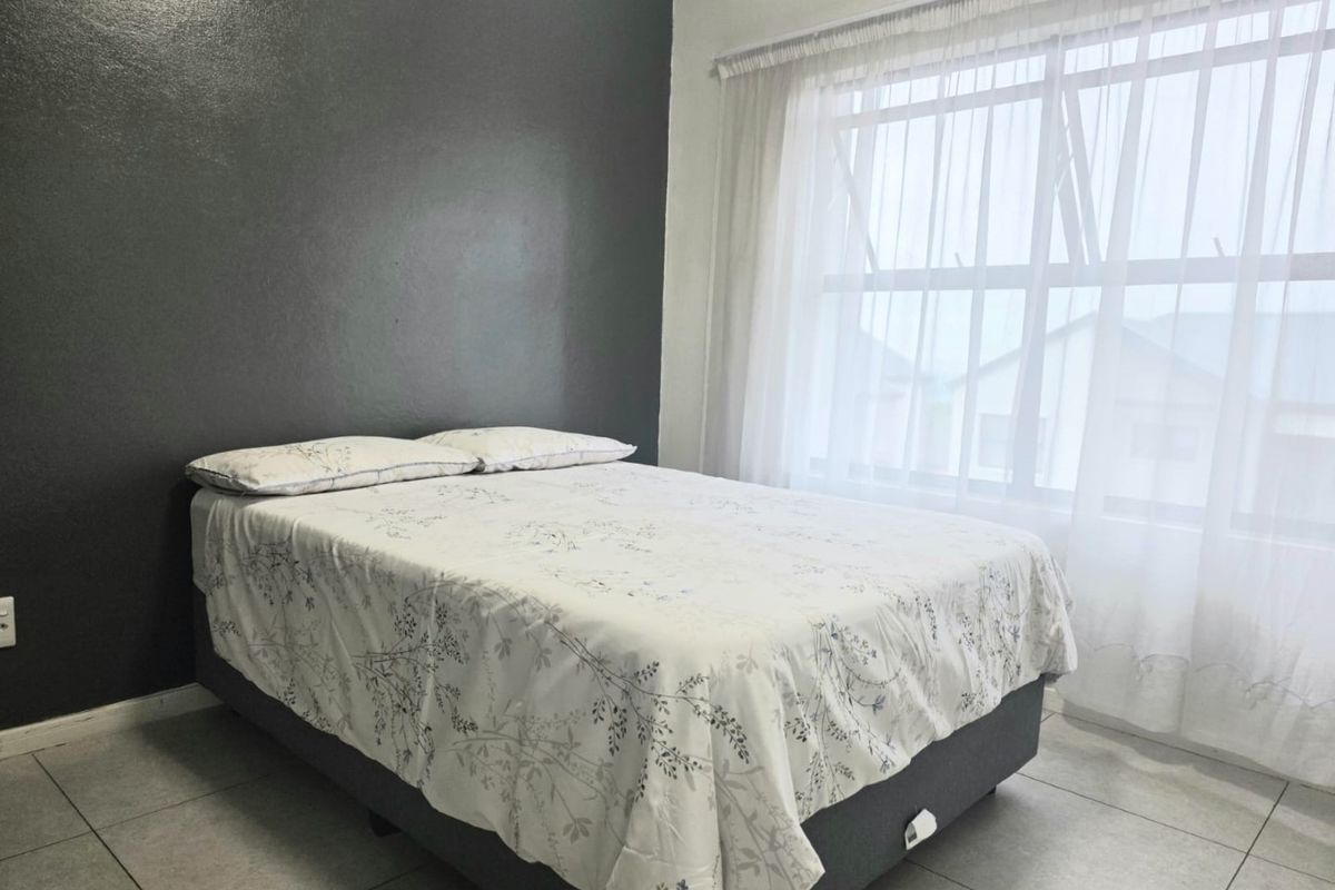 A bedroom featuring tiled flooring, a large window with sheer curtains, and a dark grey accent wall.