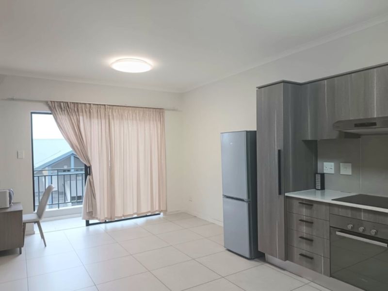 Modern open-plan kitchen and living area featuring sleek cabinetry, integrated appliances, tiled flooring, and direct access to a private balcony.