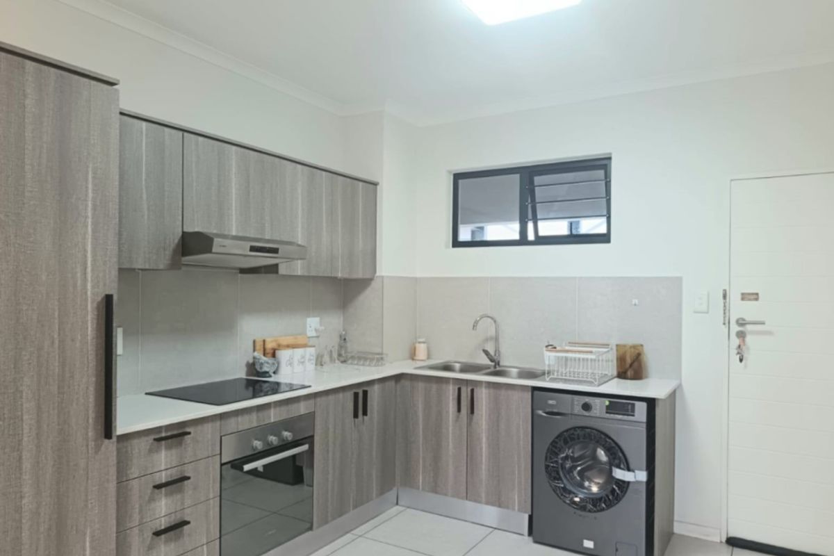 Modern kitchen featuring wood-grain cabinetry, stone-look countertops, integrated electric hob and oven, double sink, and tiled flooring with a neutral backsplash.