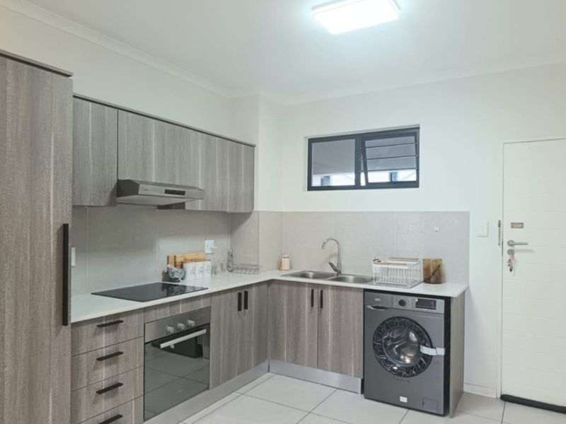 Modern kitchen featuring wood-grain cabinetry, stone-look countertops, integrated electric hob and oven, double sink, and tiled flooring with a neutral backsplash.