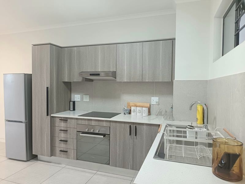 Modern kitchen featuring light wood-grain cabinetry, stone countertops, integrated electric hob, oven, extractor fan, and a stainless steel sink with a mixer tap.