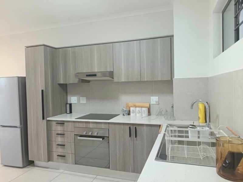 Modern kitchen featuring wood-grain cabinetry, stone countertops, integrated electric hob, oven, extractor fan, and a stainless steel sink with a mixer tap.