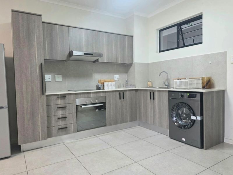 Modern kitchen featuring wood-grain cabinetry, stone countertops, integrated oven and hob, stainless steel sink, and tiled finishes throughout.