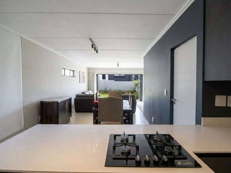Modern open-plan living area featuring a sleek kitchen with a gas hob, flowing seamlessly into a dining and lounge space with access to the garden.
