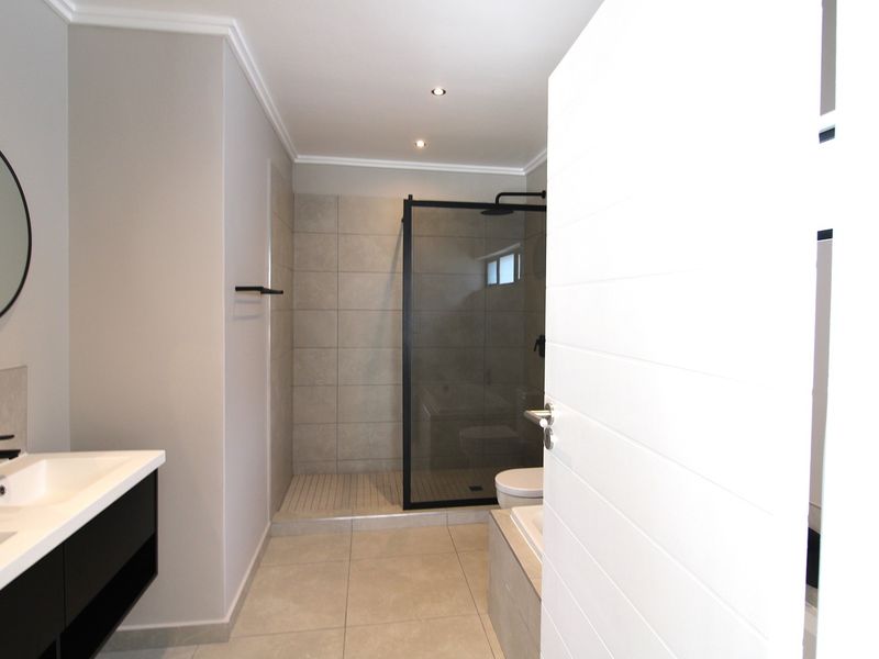 Modern bathroom featuring a double vanity, walk-in shower with black frame, and neutral floor-to-ceiling tiling.