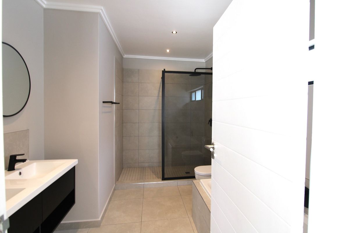 Modern bathroom featuring a double vanity, walk-in shower with black frame, and neutral floor-to-ceiling tiling.