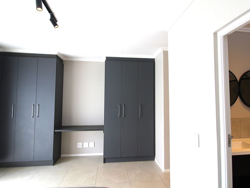 Modern bedroom featuring dark grey built-in cupboards with an integrated desk, tiled flooring, and direct access to an en-suite bathroom.