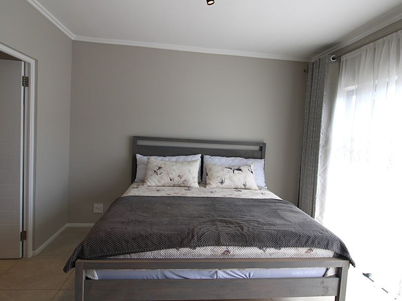 A well-maintained bedroom featuring neutral wall tones, tiled flooring, and a sliding door providing natural light.