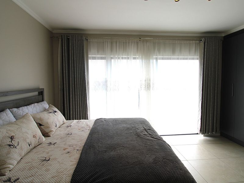 A well-maintained bedroom featuring neutral tiled flooring, built-in cupboards, and a sliding door providing access to the outdoors.