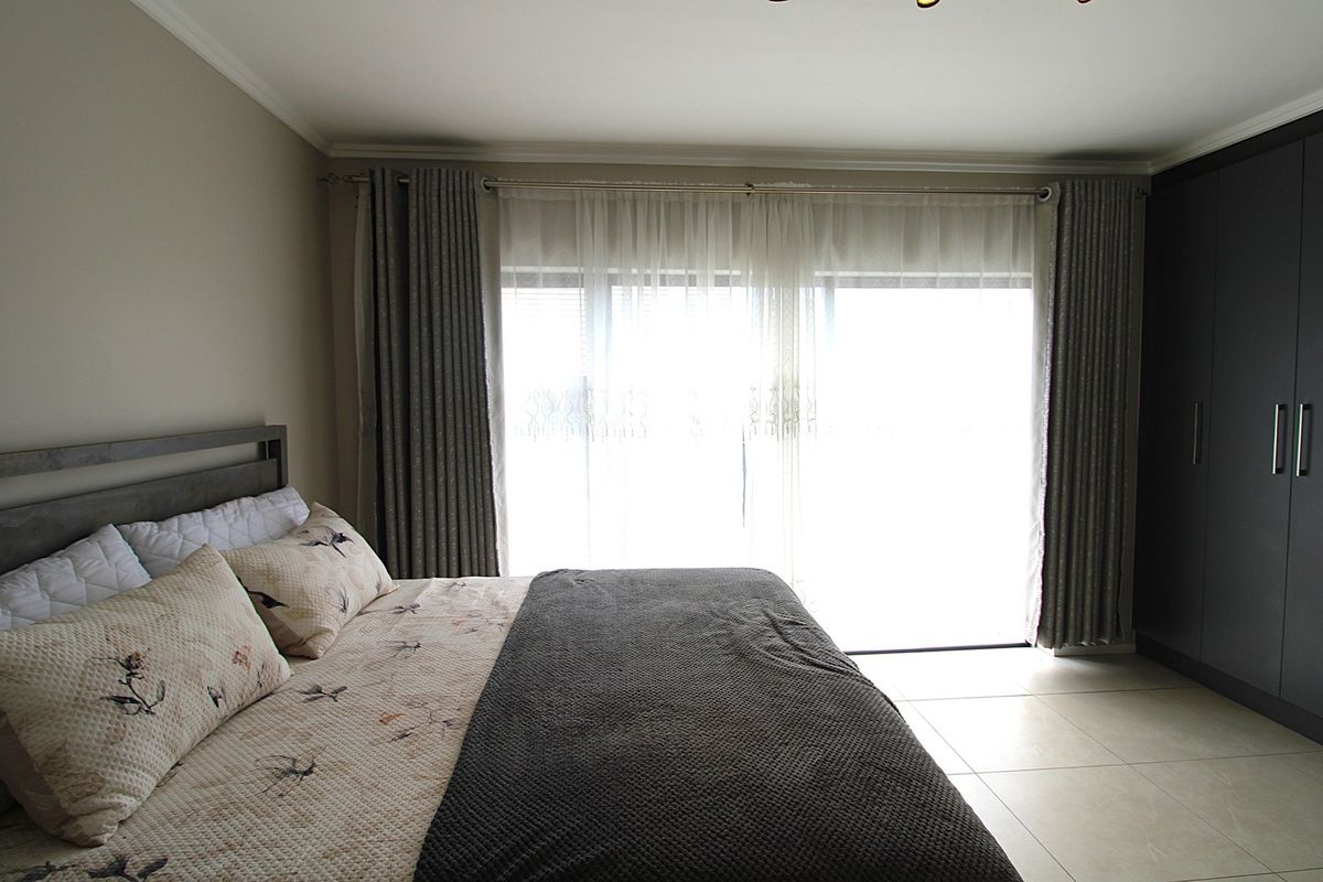 A well-maintained bedroom featuring neutral tiled flooring, built-in cupboards, and a sliding door providing access to the outdoors.