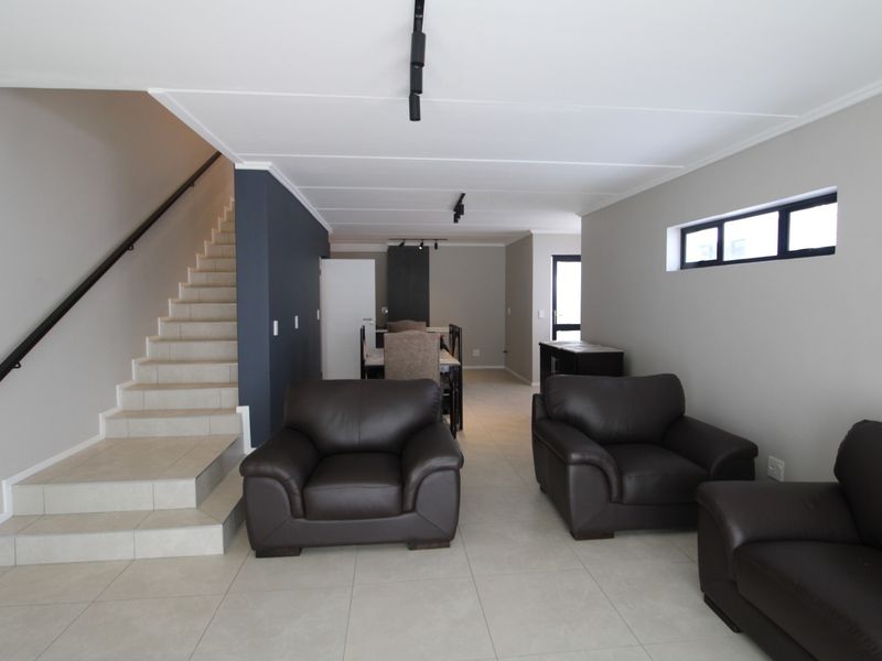 Spacious open-plan living area featuring neutral tiled flooring, a modern staircase with a metal handrail, and contemporary track lighting throughout the space.