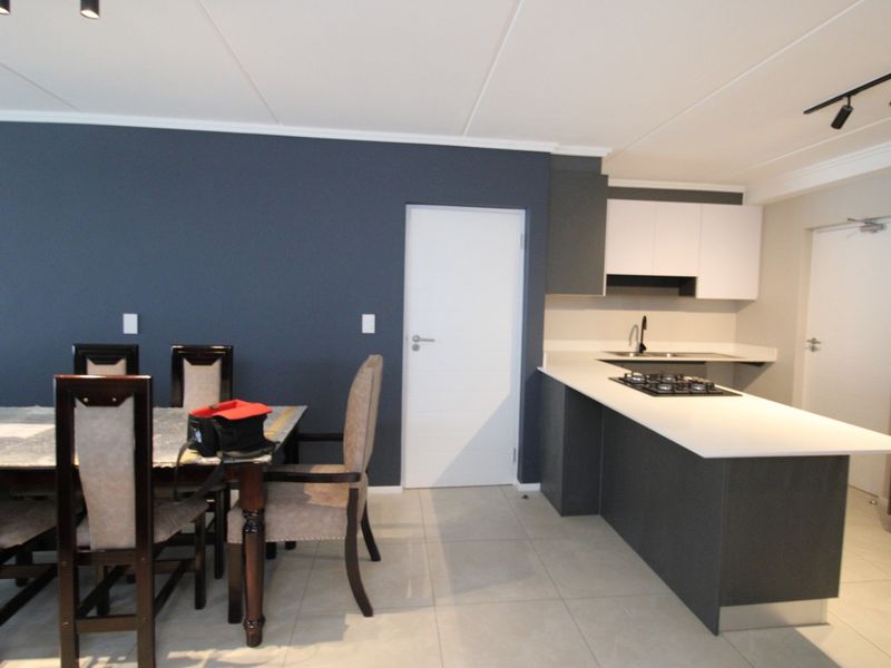 Modern open-plan living and kitchen area featuring dark cabinetry, a gas hob, tiled flooring, and contemporary track lighting.