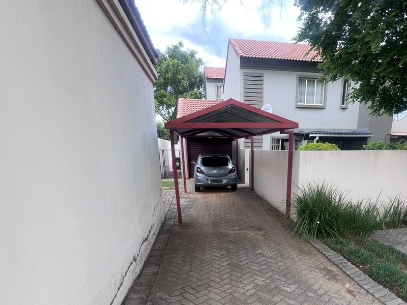 Front exterior view of the townhouse featuring a paved driveway, a covered carport, and a boundary wall.