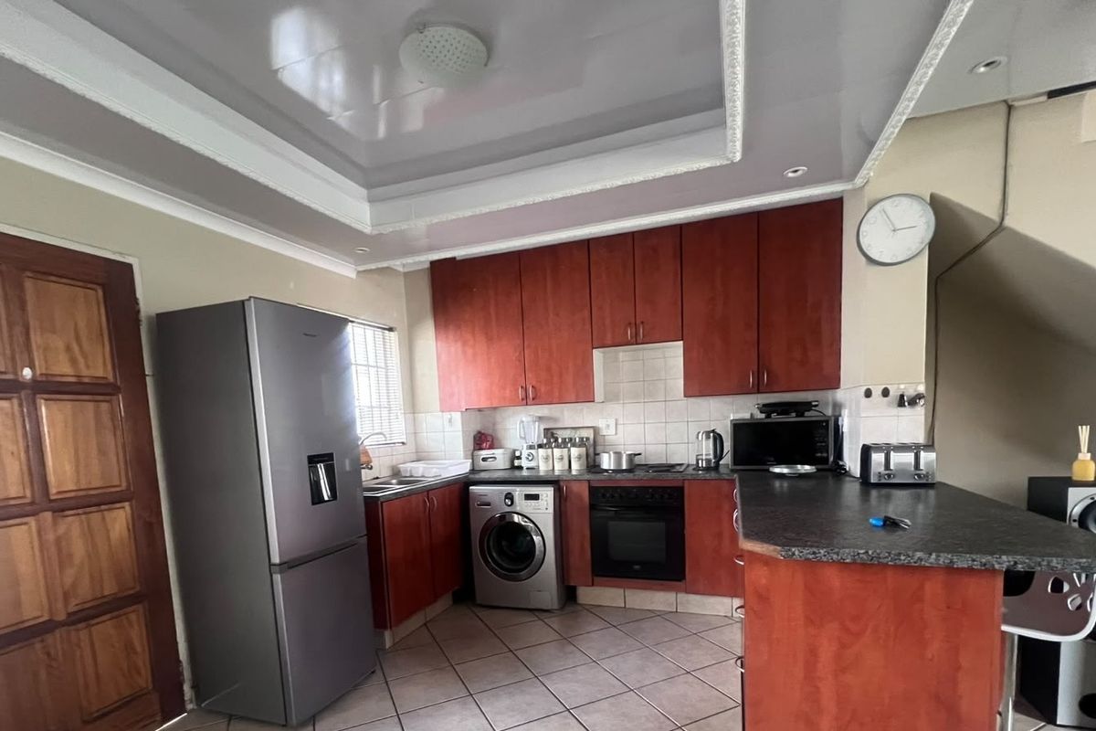 A functional kitchen featuring wood-finish cabinetry, tiled backsplash, built-in oven and hob, and a breakfast counter, with a distinctive recessed ceiling design.